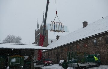 Spektakuläre Ankunft bei Schneetreiben: Am Haken eines Krans schweben die Glaselemente im Dezember 2022 vom Domänenhof aus an den Türmen des Westwerks vorbei.