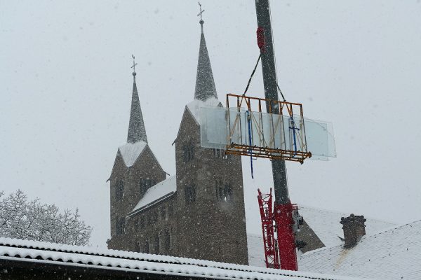 Spektakuläre Ankunft bei Schneetreiben: Am Haken eines Krans schwebten die Glaselemente vom Domänenhof aus an den Türmen des Westwerks vorbei.